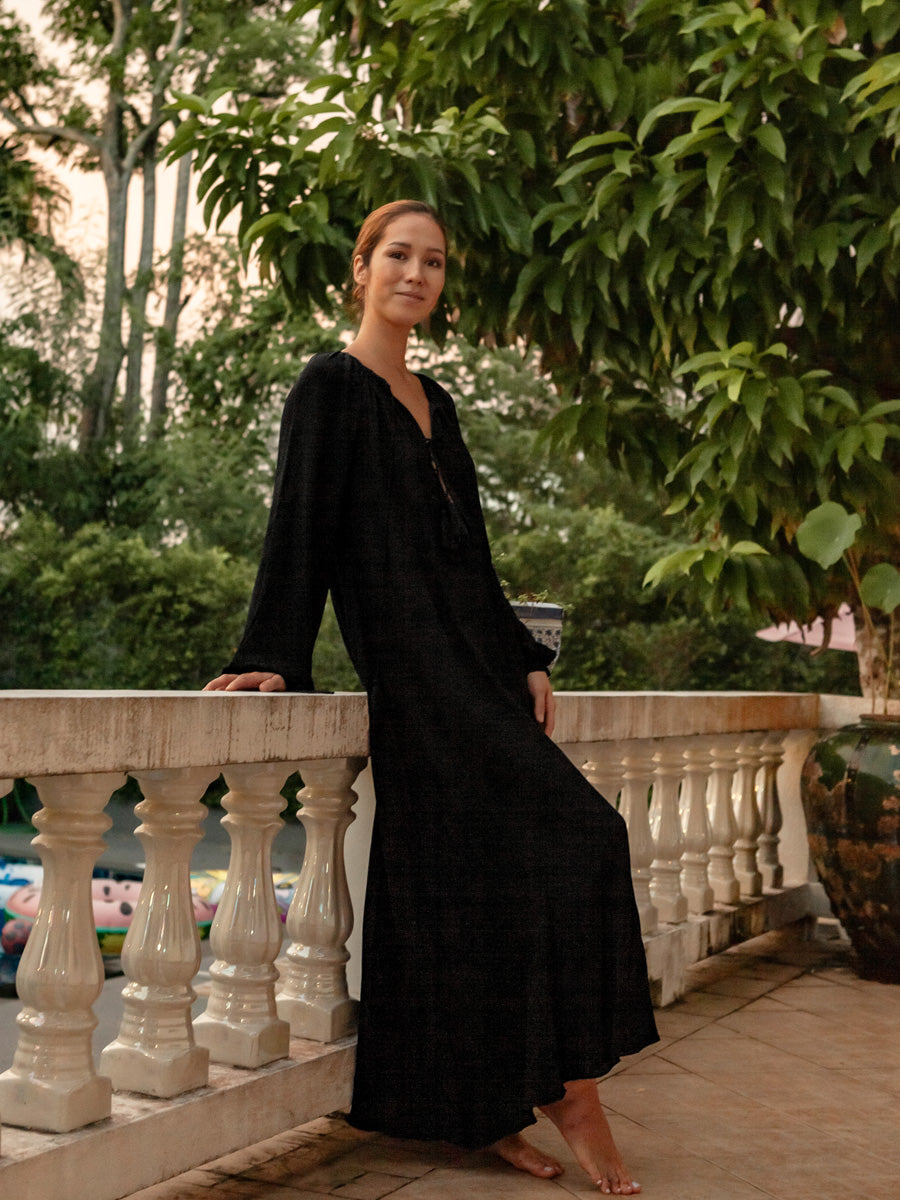 Woman in a black dress standing on a balcony with greenery in the background